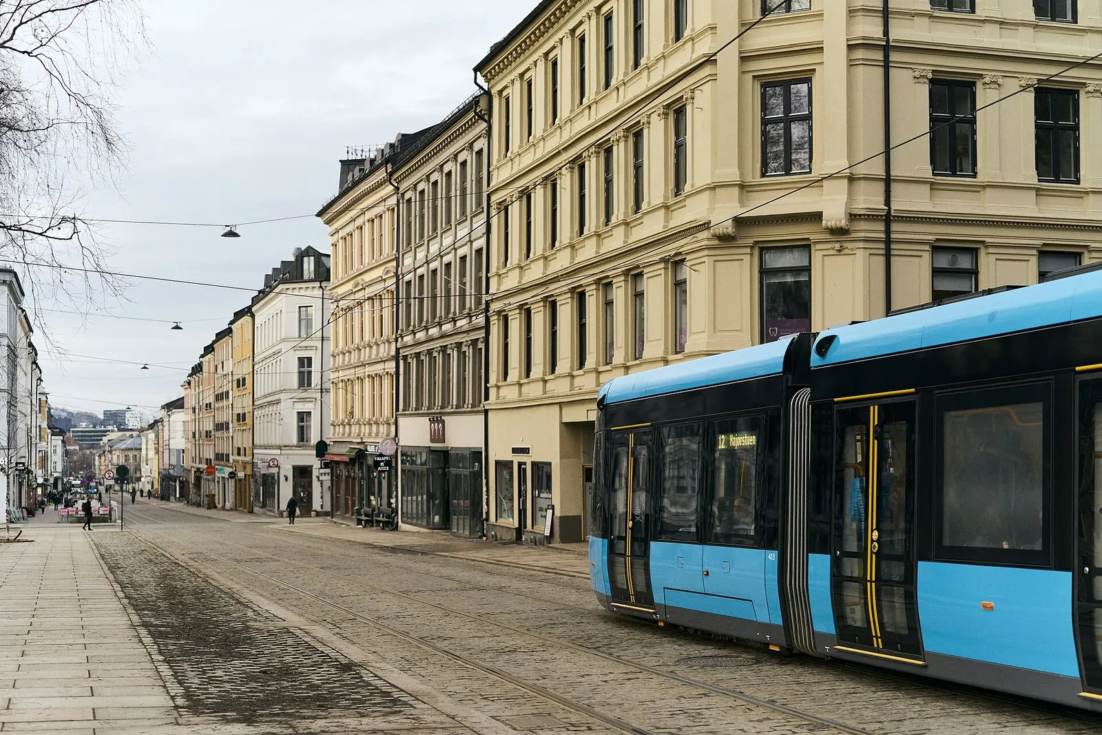 Rue pavée bordée d'immeubles anciens aux façades claires, avec un tramway bleu qui passe sur les rails