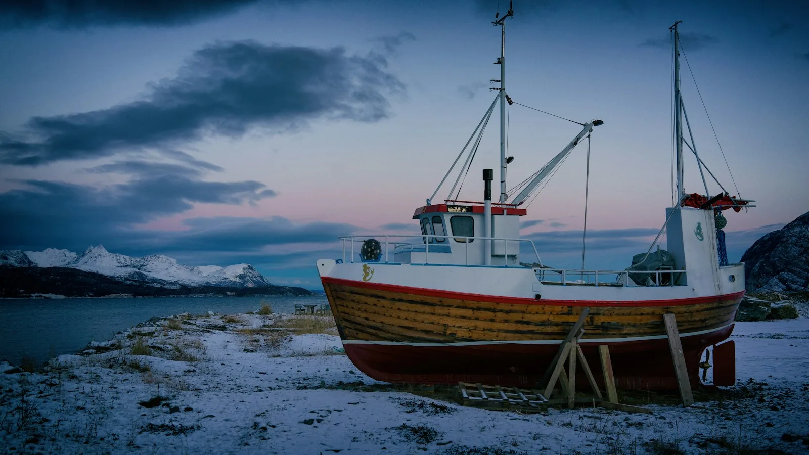 Bateau de pêche en bois au bord d'un fjord enneigé du Finnmark, en Norvège