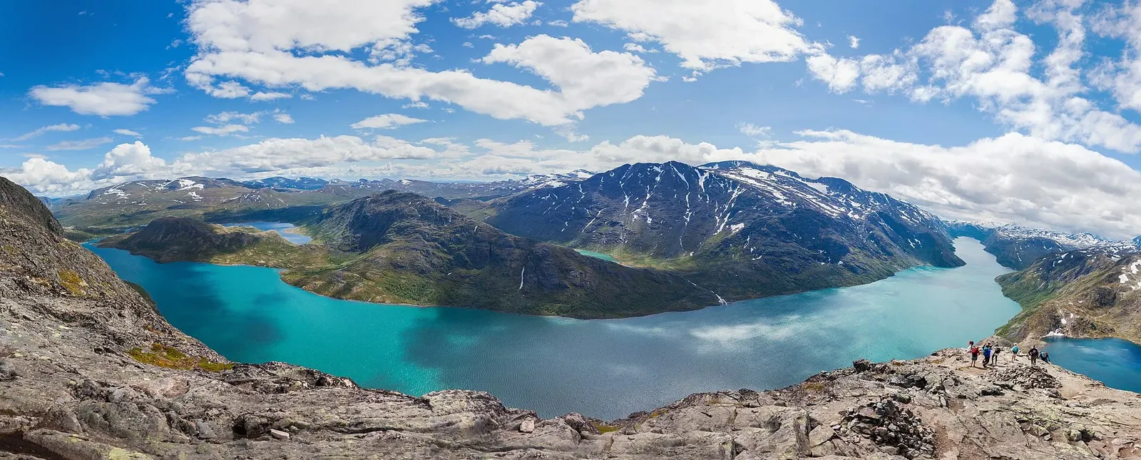 Vue panoramique depuis la crête de Besseggen sur un lac turquoise, des montagnes enneigées et des randonneurs