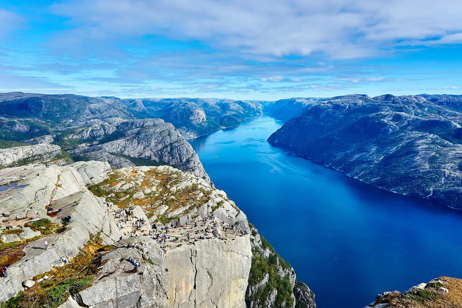 Le plateau rocheux du Preikestolen et sa falaise abrupte dominant un fjord bleu, avec des randonneurs sur le rebord